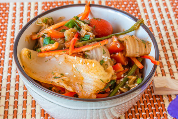 Spicy Asian salad of pickled Chinese cabbage, tomatoes, pepper, green onions and sesame. Kimchi cabbage in a bowl on a bamboo napkin.