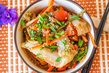 Spicy Asian salad of pickled Chinese cabbage, tomatoes, pepper, green onions and sesame. Kimchi cabbage in a bowl on a bamboo napkin.