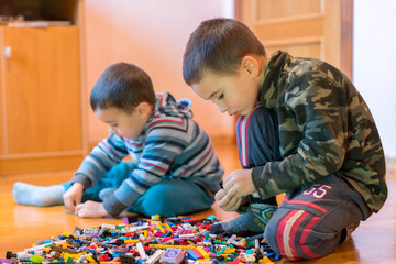 Two children playing with lots of colorful plastic blocks constructor sitting on a floor indoor. Two little brothers play constructor. Communication and friendship