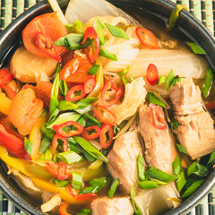 Suan cai - soup, stew of pork and pickled Chinese cabbage in a black bowl on a bamboo napkin, close-up, top view. Northeastern сhinese cuisine.