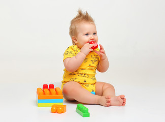 Смешной пухлый 9 месячный малыш с прической в желтой одежде сидит на белом фоне с игрушками