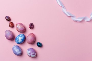 Stylish colorful eggs and quail eggs with white ribbon on pink background, copy space.Happy Easter concept