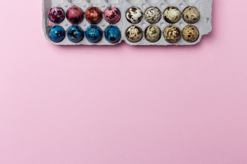 Colored quail eggs in box on pink background