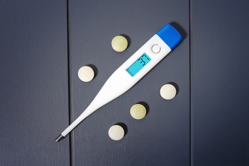 Electronic thermometer with pills and medicines to reduce heat. First aid and flu fever symptoms