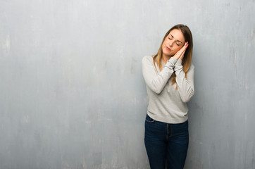 Young woman on textured wall making sleep gesture in dorable expression