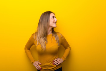 Obraz premium Young woman on yellow background posing with arms at hip and laughing