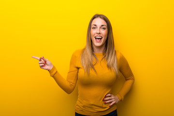 Young woman on yellow background pointing finger to the side and presenting a product