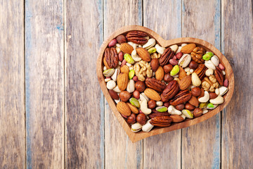 Heart shaped bowl with mixed nuts on wooden table top view. Healthy food and snack.