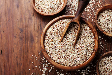 Raw mixed quinoa in bowl on wooden kitchen table top view. Healthy and diet superfood product.