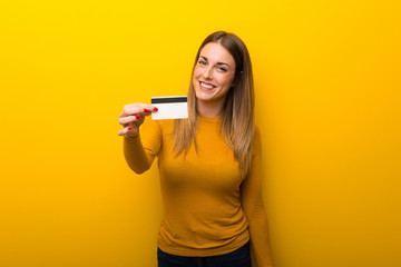Young woman on yellow background holding a credit card