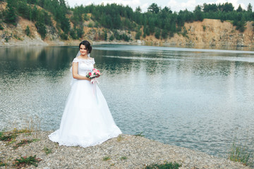 Fototapeta na wymiar A beautiful bride in a snow-white dress stands near a blue clean lake