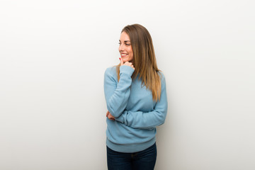 Blonde woman on isolated white background looking to the side with the hand on the chin