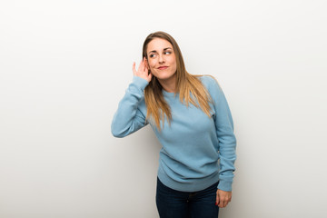 Blonde woman on isolated white background listening to something by putting hand on the ear