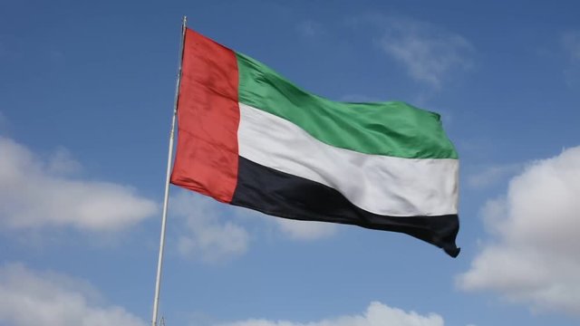 United Arab Emirates (UAE) Flag blowing in the wind on a beautiful blue sky day with puffy white clouds. 