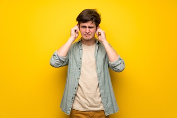 Teenager man over yellow wall covering ears with hands. Frustrated expression