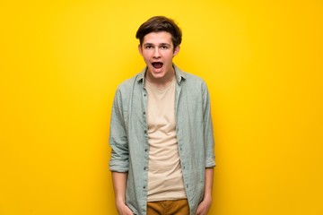 Teenager man over yellow wall with surprise and shocked facial expression