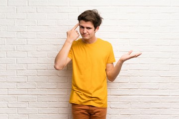 Teenager man over white brick wall making the gesture of madness putting finger on the head