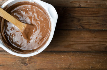 Cake pan with chocolate batter and wooden spoon close up on dark wooden background.