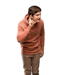 Teenager man with sweatshirt listening to something by putting hand on the ear over isolated white background