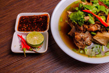 Cow bone soup or Sup Tulang in Malay with chilli and soya sauce . Muslim food in white bowl on dark brown wooden plate . Selective focus .