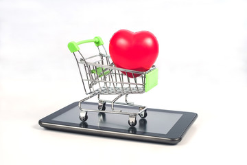 Shopping cart or metal trolley on mobile tablet with heart for Online shopping and ecommerce.