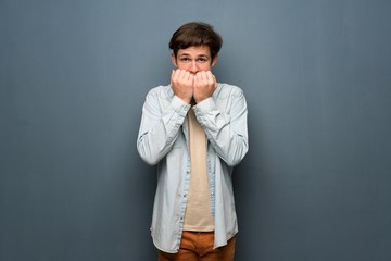 Teenager man with jean jacket over grey wall nervous and scared putting hands to mouth
