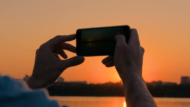 Man taking photo of beautiful sunset with smartphone in city. Sunset light, golden hour. Photography, nature and journey concept. Close up shot of man hands with phone