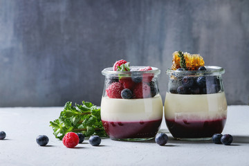 Homemade classic dessert Panna cotta with raspberry and blueberry berries and jelly in jars, decorated by mint, sugar powder, honey combs over white blue table