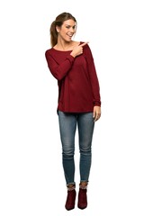 A full-length shot of a Blonde woman pointing to the side to present a product over isolated white background