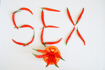 Half a tomato and red hot chili peppers lie on a white surface. Vegetables make up the word Sex. Seasoning and health