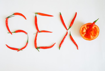 Half a tomato and red chili peppers lie on a white background. Vegetables make up the word Sex. Seasoning and health