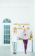 Senior woman and blonde girl in cook costumes in kitchen eating fresh fruit.