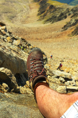 View of a boot of a resting tourist with two tourists climbing down on backgroud