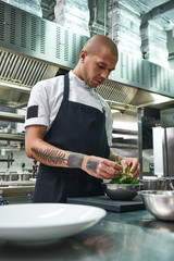 Choosing ingredients. Vertical photo of male chef in apron, with stylish tattoos on his arms...