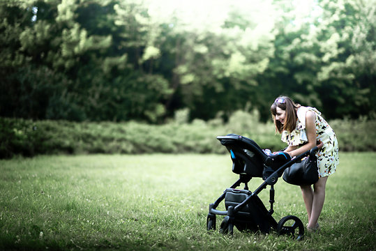 Mother walking with a baby pram (stroller, carriage) in park og the town. Love and family concept