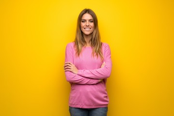 Woman with pink sweater over yellow wall keeping the arms crossed in frontal position