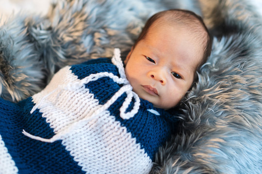 newborn baby boy swaddled in a knit wrap on fur bed