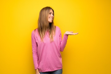Woman with pink sweater over yellow wall presenting an idea while looking smiling towards