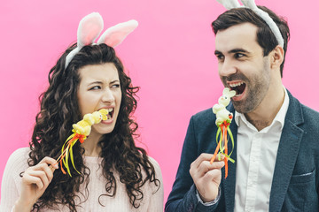 Young pretty sweet couple standing on a pink background. At the same time, there are hooves on the head. A husband and wife carefully look at each other with an open mouth put sweet bunnies in the