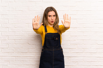 Teenager girl over white brick wall making stop gesture and disappointed