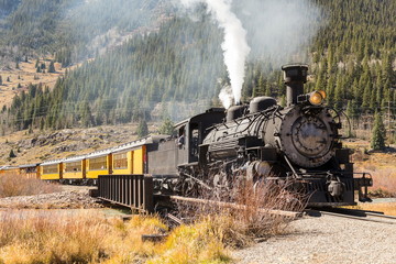 Vintage steam train with yellow wagons going uphill in mountain area