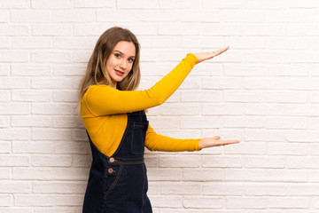 Teenager girl over white brick wall holding copyspace to insert an ad