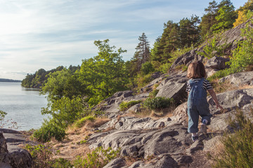 A young girl climbs over the rocks on top of a hill. A little girl climbs a mountain. Overcoming difficulties.