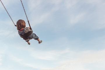 Little girl on a swing and a blue sky with some cloud.