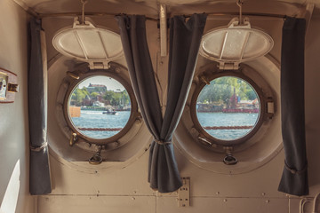 Two portholes with a view of the river and the boat.