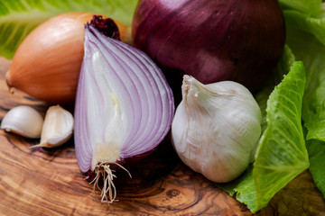 Organic Garlic, Red and Yellow Onions arranged on natural olive wood. Allium Cepa. Allium sativum.