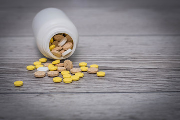 White, yellow and pink pills spilling out of a toppled bright white pill bottle. Medical colorful...