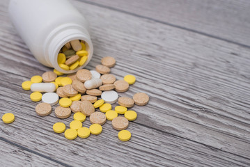 White, yellow and pink pills spilling out of a toppled bright white pill bottle. Medical colorful pills, capsules or supplements for the treatment and health care on wooden background.