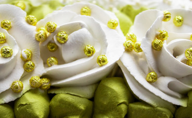 White roses and green leaves made with cream, closeup.