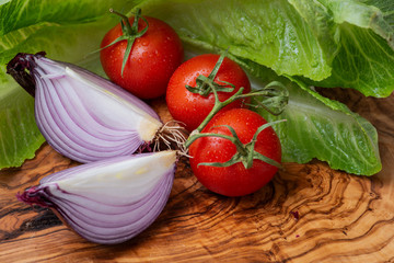 Red Onion cut into wedges and Organic Red Tomatoes on the vine arranged on natural olive wood.